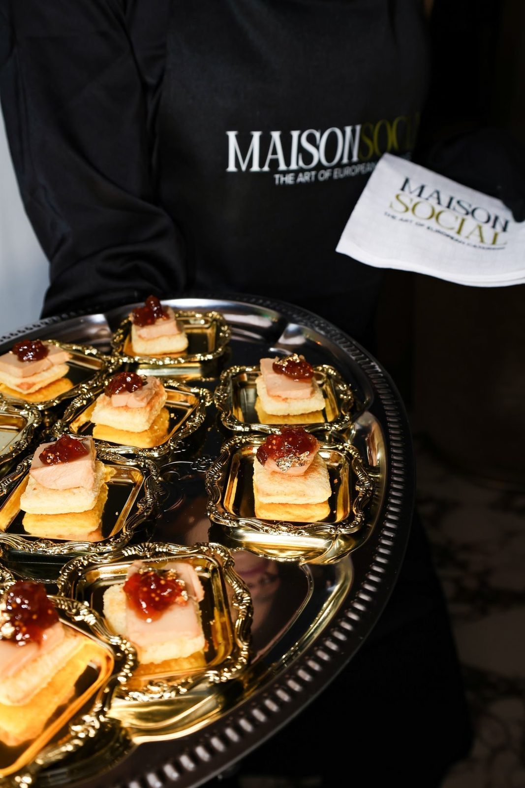 Server in a Maison Social apron with a tray of canapes